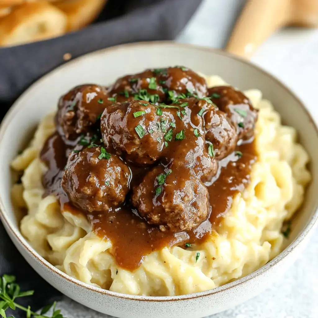 Creamy brown gravy covering pasta and meatballs, topped with parsley pieces.