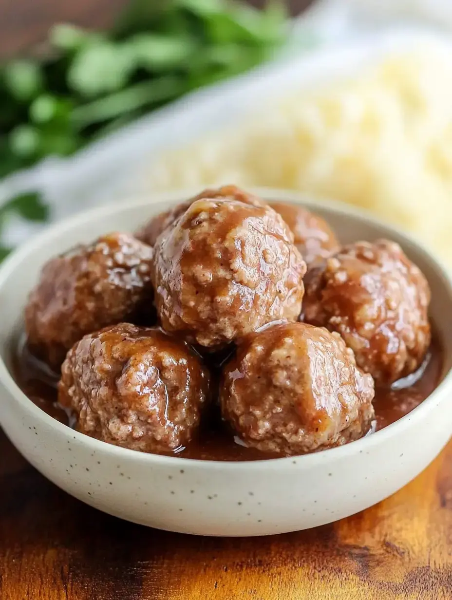 Tender meatballs swimming in rich brown gravy with fragrant herbs scattered nearby for garnish.
