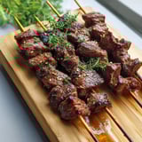 Wooden board with beef skewer resting on it.